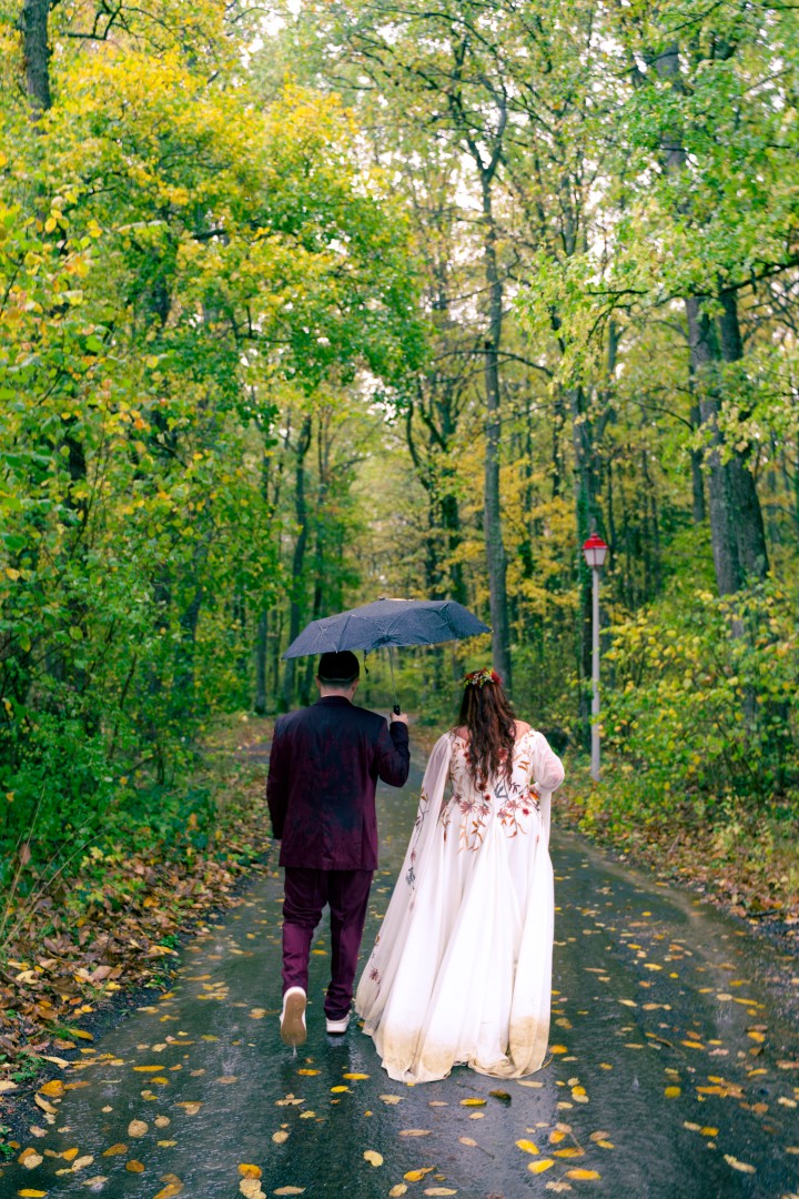 Jeunes mariés marchant sous un parapluie sur un chemin forestier d’automne