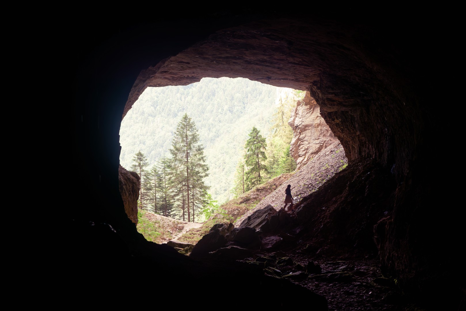 Silhouette à l’entrée d’une caverne ouverte sur la forêt, en Chartreuse
