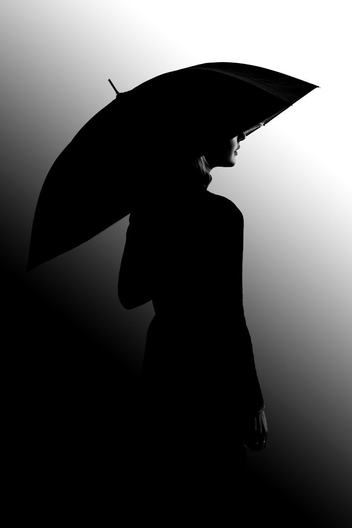 Silhouette d'une personne sous un parapluie en contre-jour très contrasté